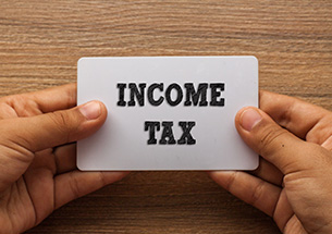 INCOME TAX written on card with hand holding it with wood background